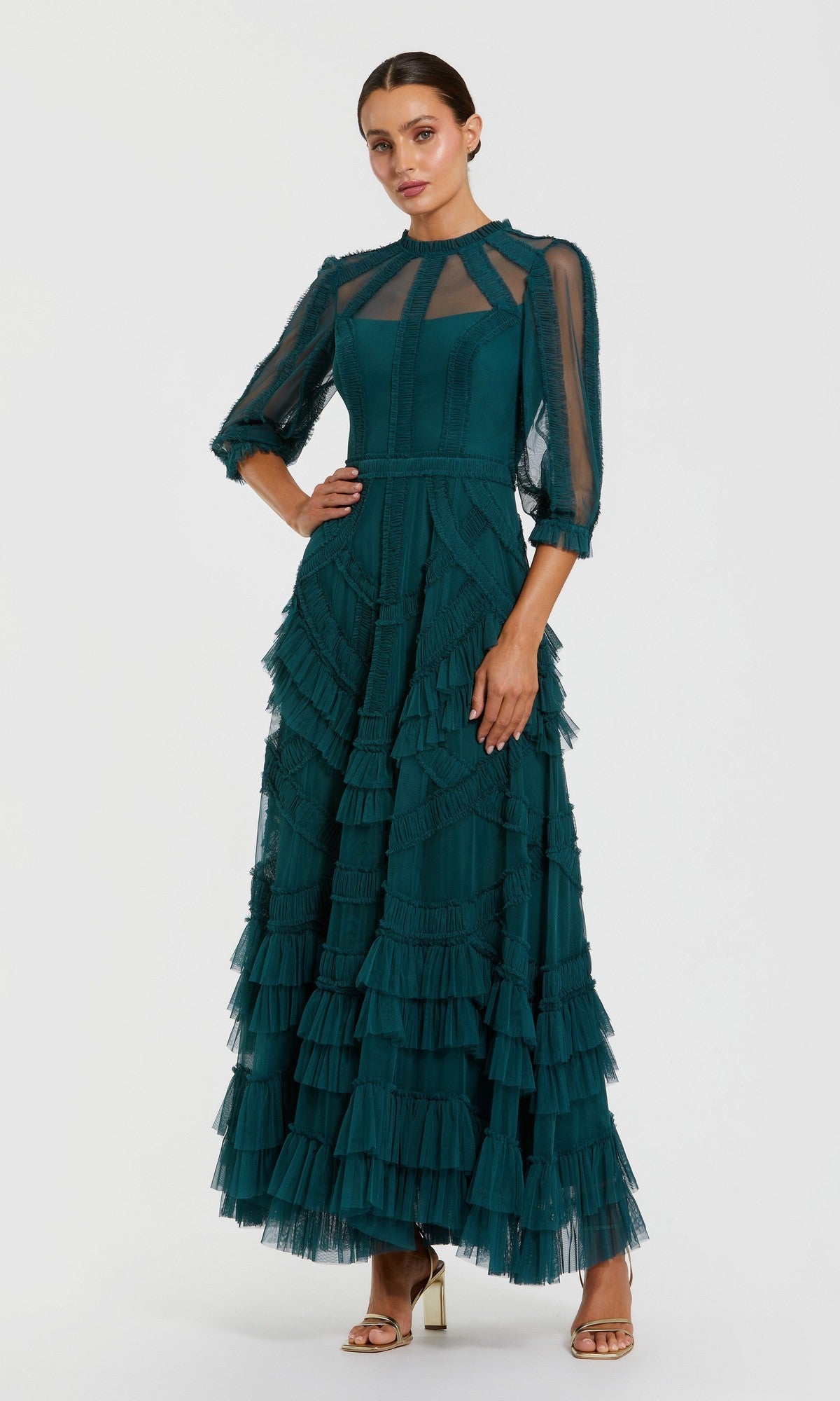 A woman in the Mac Duggal 8251 long formal dress in teal, featuring mesh fabric, sheer sleeves, and layered ruffles, stands in heels against a plain backdrop.